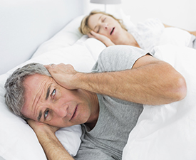 Fed up man blocking his ears from noise of wife snoring at home in bedroom